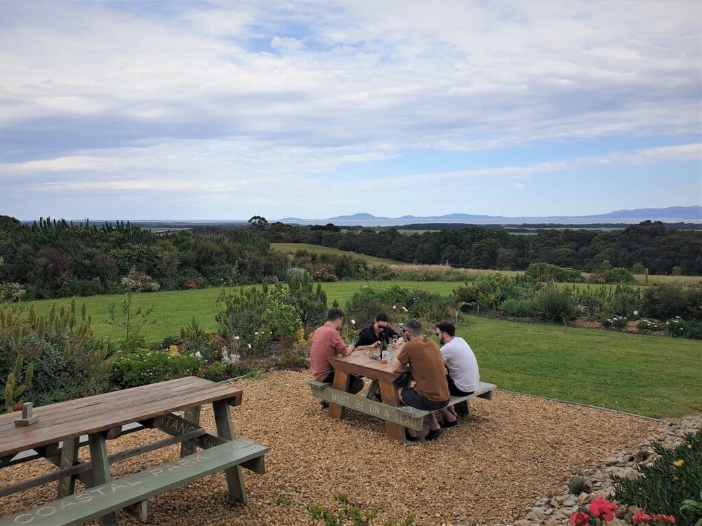 a group of people sitting at a wooden picnic table overlooking lush green pastures