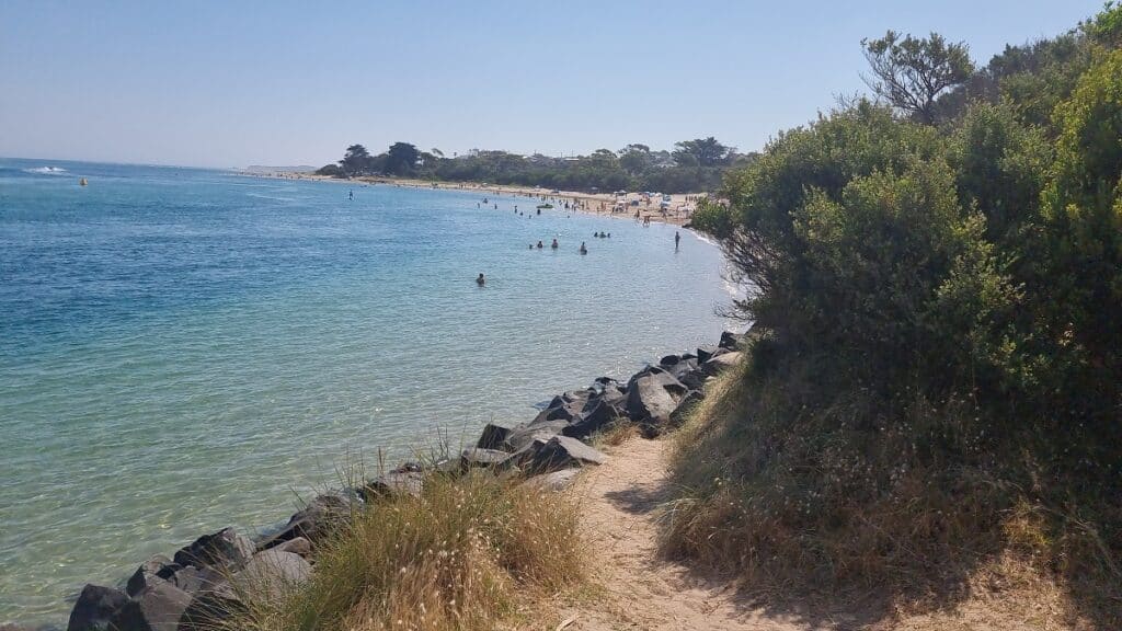 A calm beach at Inverloch with rocks and scrub surrounding the shoreline.